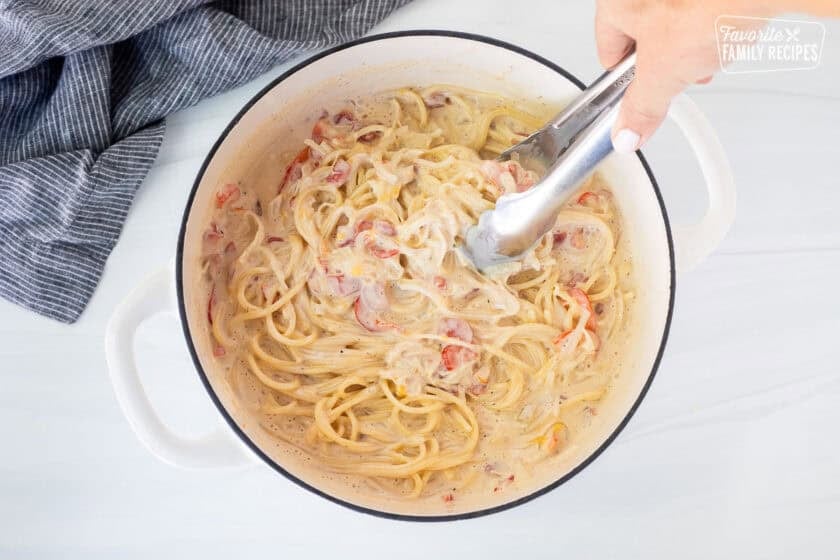 Combining spaghetti noodles with sauce using tongs in dutch oven.