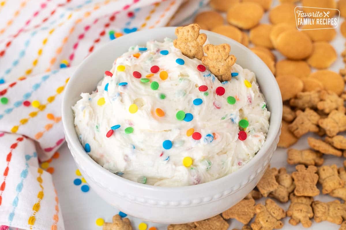 Dunkaroo dip in a bowl with extra sprinkles and teddy grahams on top. Teddy grahams and mini Nilla wafers on the side.