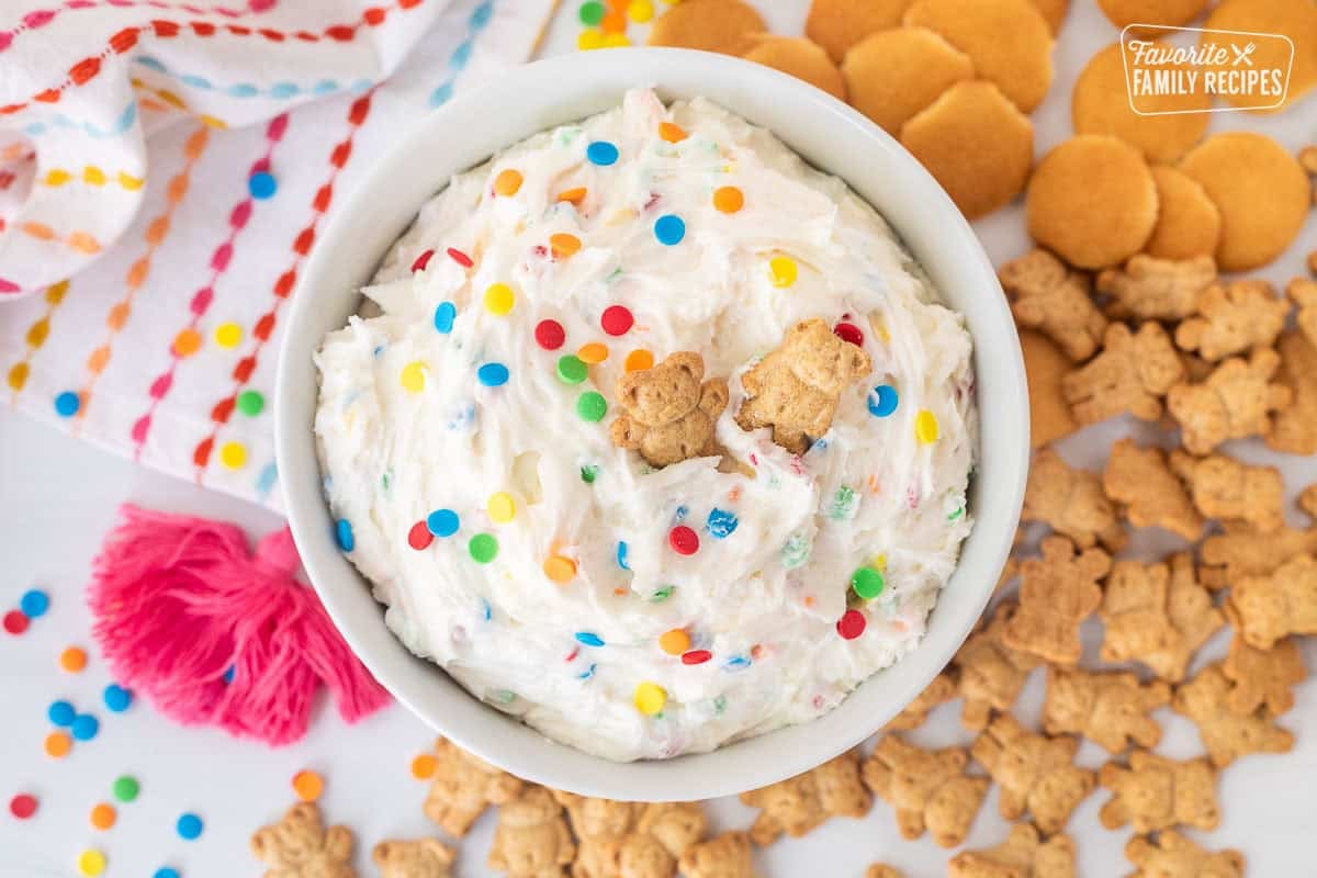 Dunkaroo dip in a bowl with extra sprinkles and teddy grahams on top. Teddy grahams and mini Nilla wafers on the side.