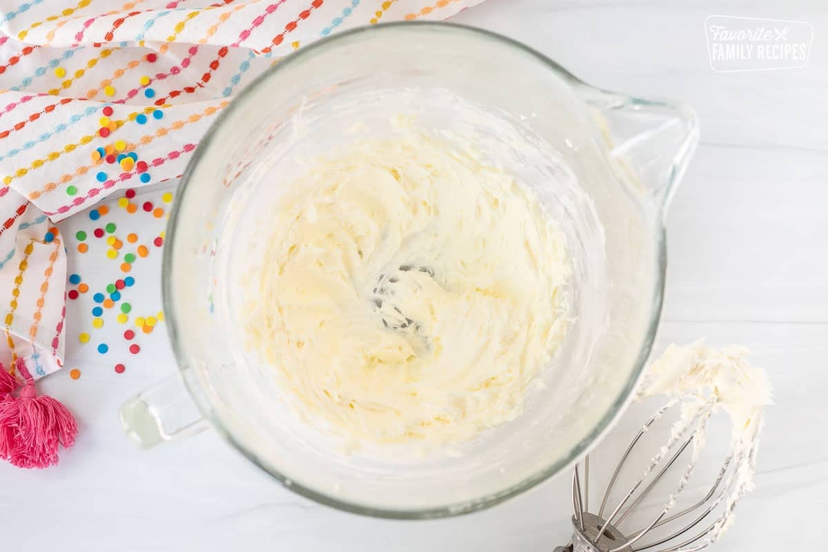 Glass mixing bowl with creamed butter and whisk attachment on the side.