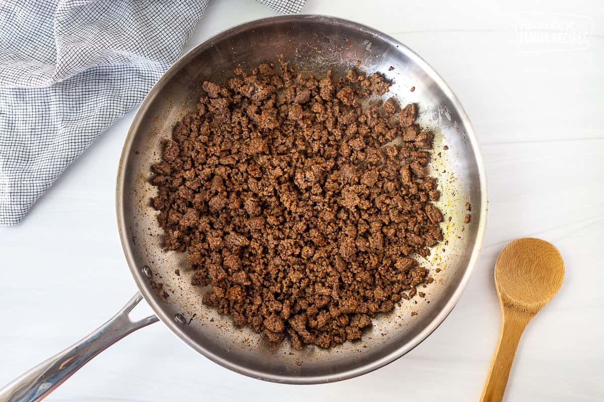 Skillet with browned ground beef and seasonings. Wooden spoon on the side.