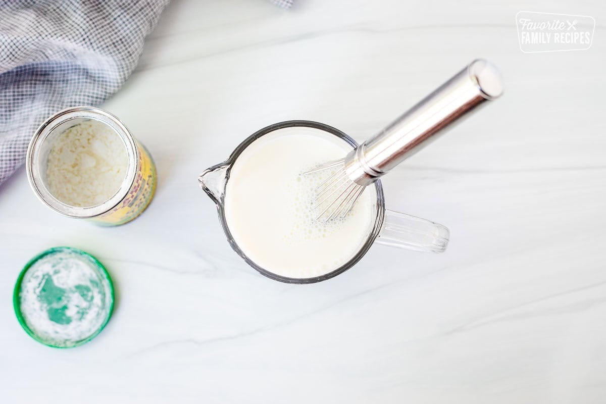 Small glass mixing bowl with milk and cornstarch being mixed with a whisk.