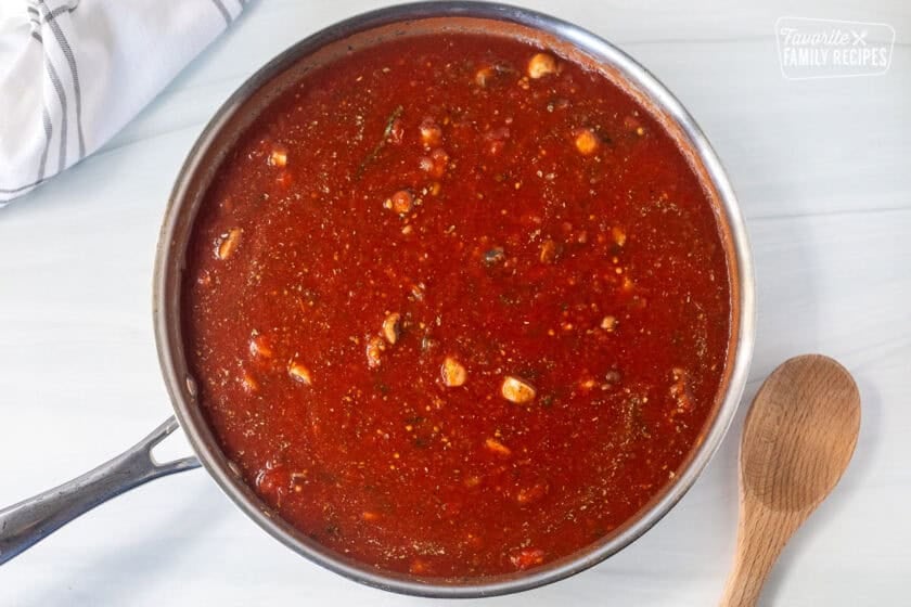 Skillet with sauce ingredients added for simmering. Wooden spoon on the side.
