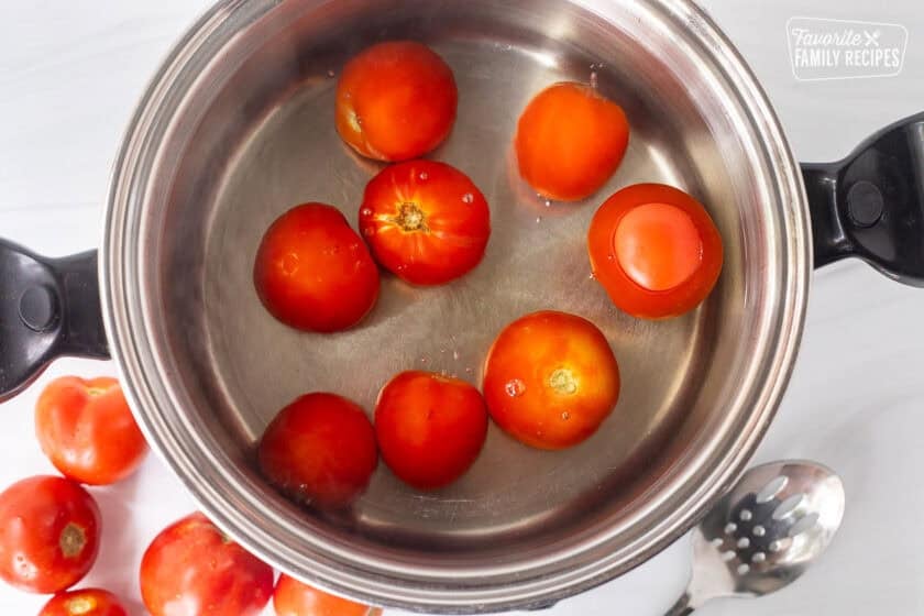 Large pot of boiling water with tomatoes and slotted spoon on the side.