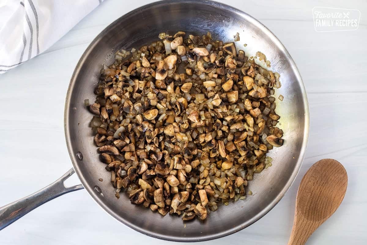 Sautéing mushrooms and onions in a frying pan to make a spaghetti sauce