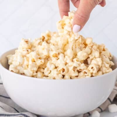 Hand picking up a piece of marshmallow popcorn from bowl.