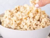 Hand picking up a piece of marshmallow popcorn from bowl.