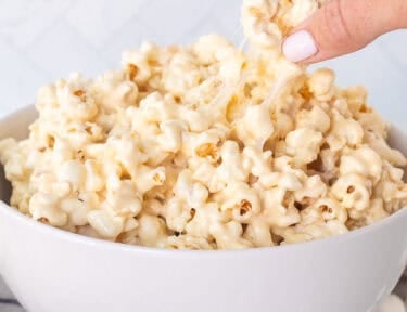 Hand picking up a piece of marshmallow popcorn from bowl.
