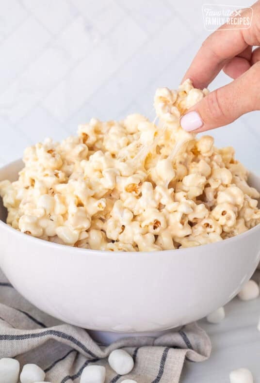 Hand picking up a piece of marshmallow popcorn from bowl.