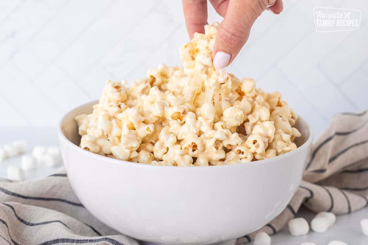 Hand picking up a piece of marshmallow popcorn from bowl.