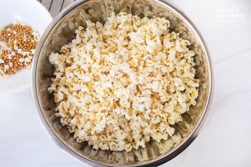 Popped popcorn in a large bowl with unpopped kernels on the side.