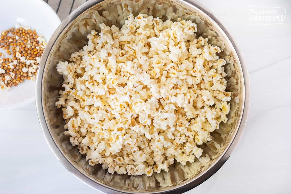 Popped popcorn in a large bowl with unpopped kernels on the side.