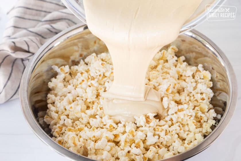 Pouring melted marshmallow mixture into large bowl of popped popcorn.