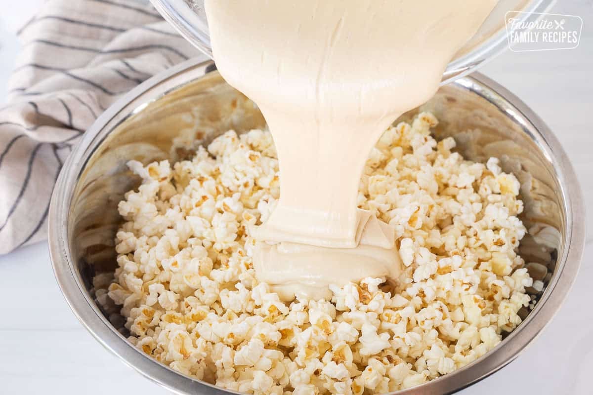 Pouring melted marshmallow mixture into large bowl of popped popcorn.