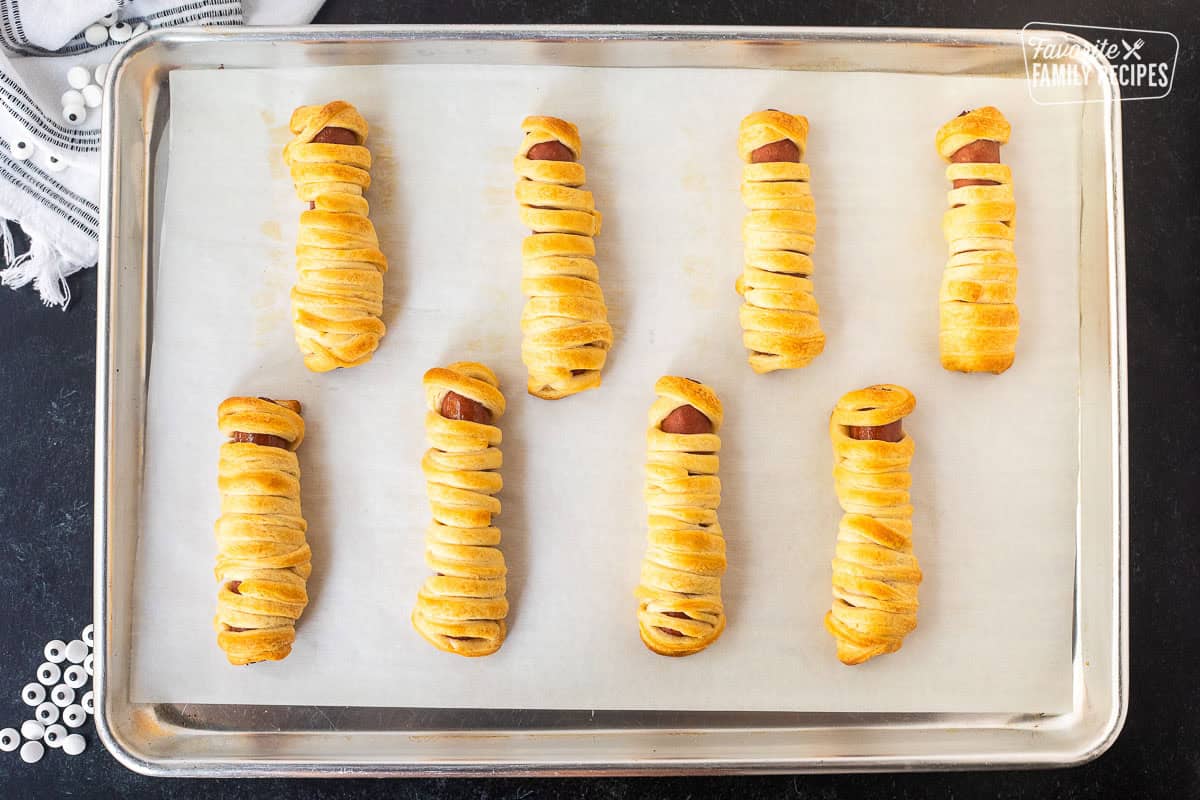 Sheet pan with baked hot dogs wrapped in strips of crescent roll.
