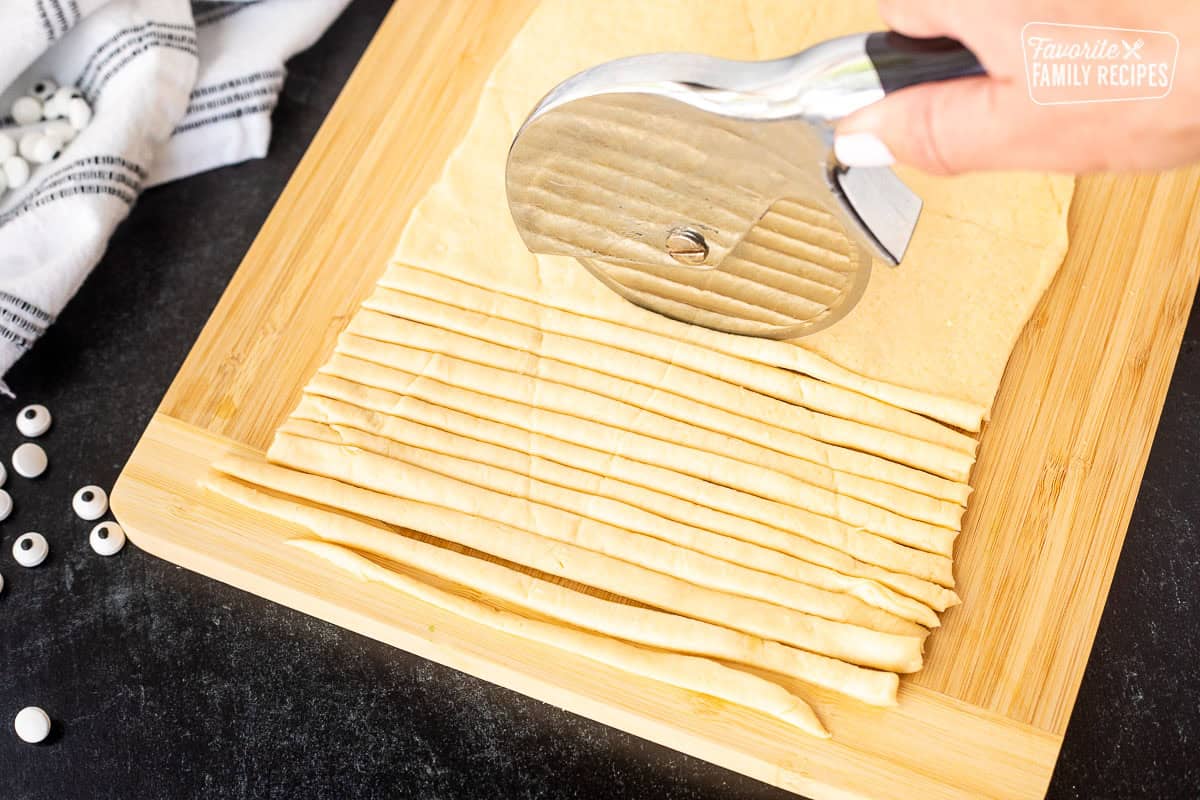 Slicing crescent roll sheet into thin strips using a pizza cutter.