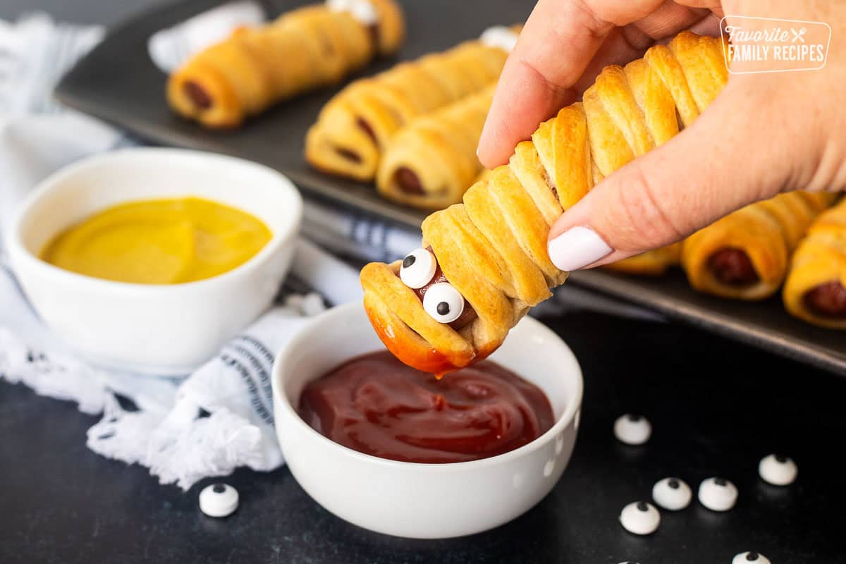 Dipping a mummy hot dog into ketchup.