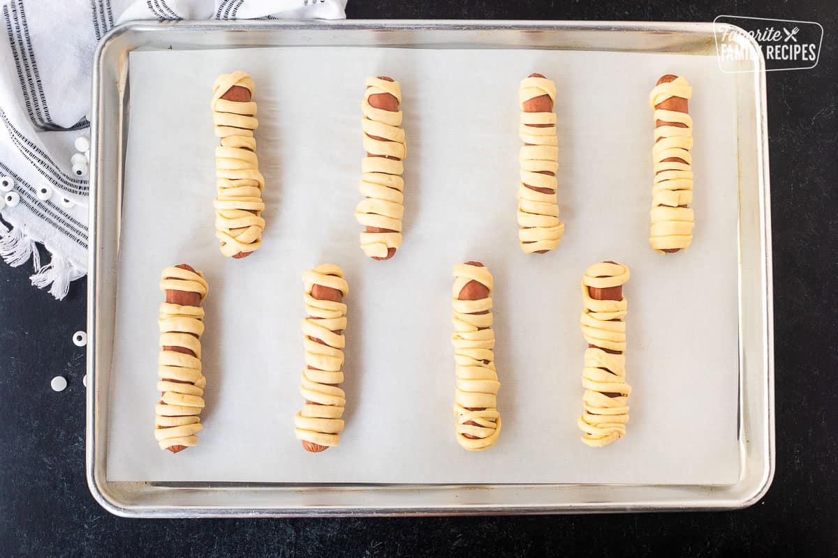 Lined baking sheet with wrapped hot dogs in crescent rolls.