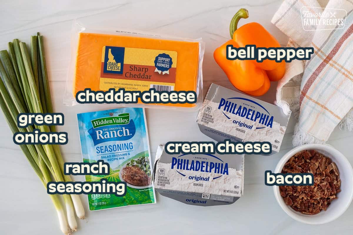 Ingredients to make a Pumpkin Shaped Cheese Ball including sharp cheddar cheese, bell pepper, cream cheese, bacon, ranch seasoning packet and green onions.