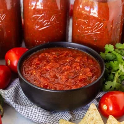 Bowl of savory canned salsa next to jars of salsa and chips on the side.