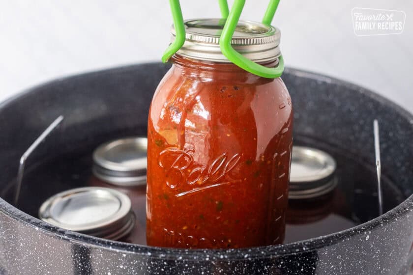 Lifting hot savory canned salsa with jar lifter from canning pot.