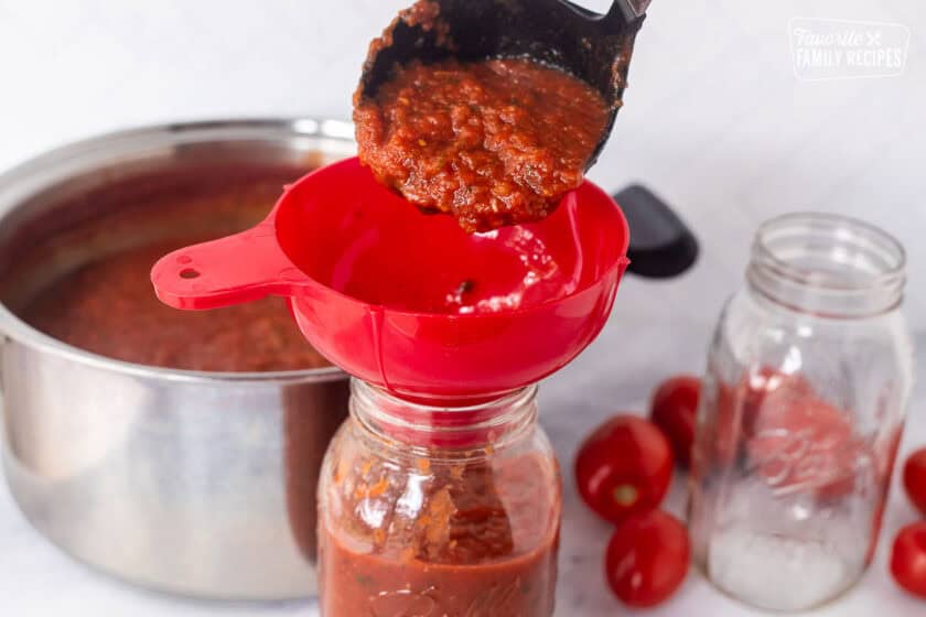 Pouring savory salsa into canning funnel to fill jars.