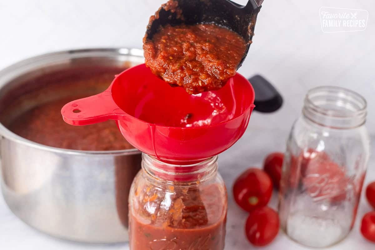 Pouring savory salsa into canning funnel to fill jars.