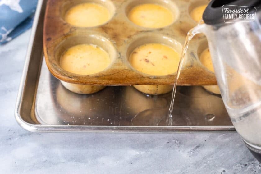 Pouring hot water into cookie sheet under the muffin pan of uncooked egg bites.