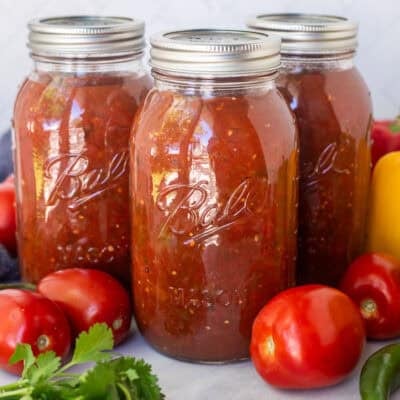 Jars of sweet canned salsa surrounded by fresh vegetables.