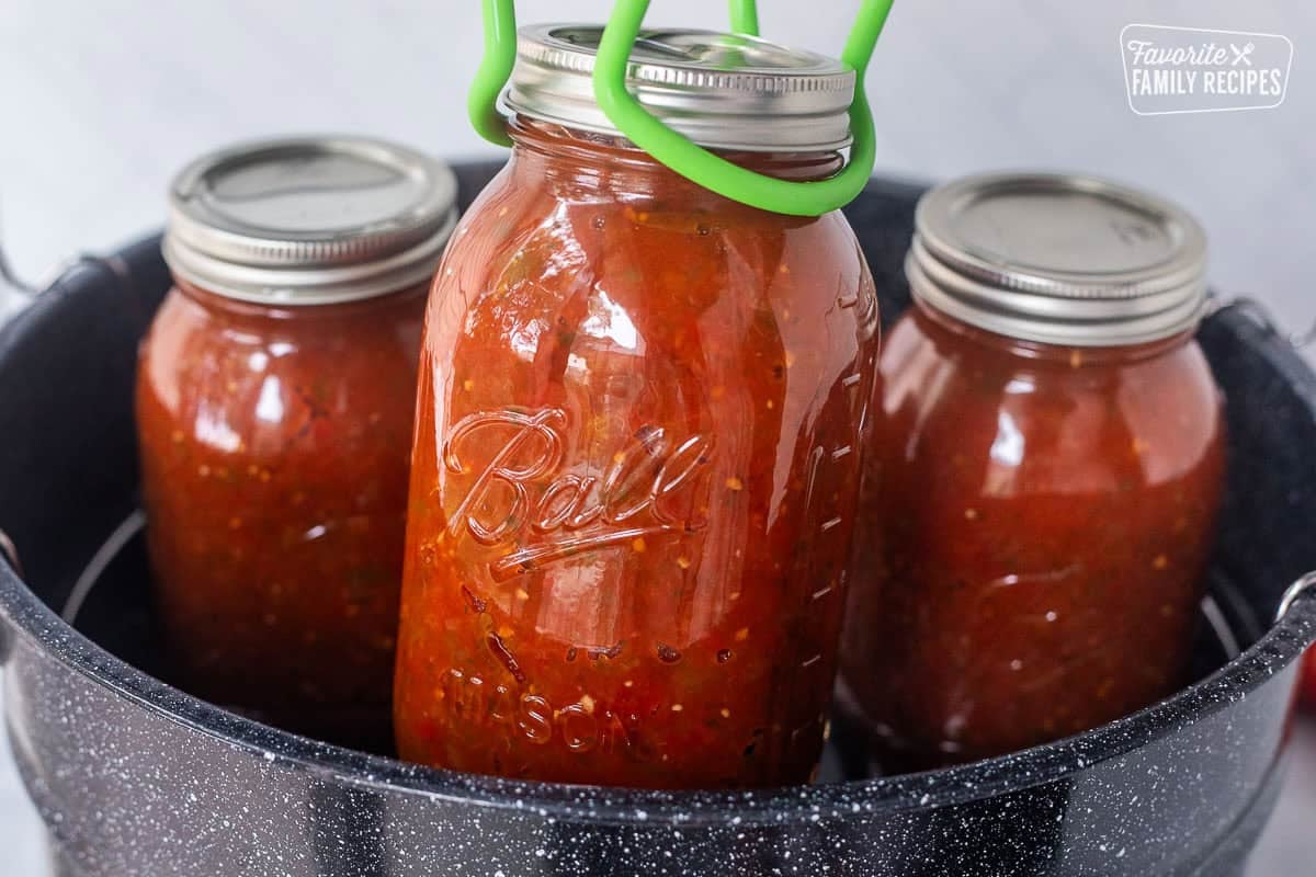 Lifting a jar of sweet canned salsa from a canning pot with a jar lifter.