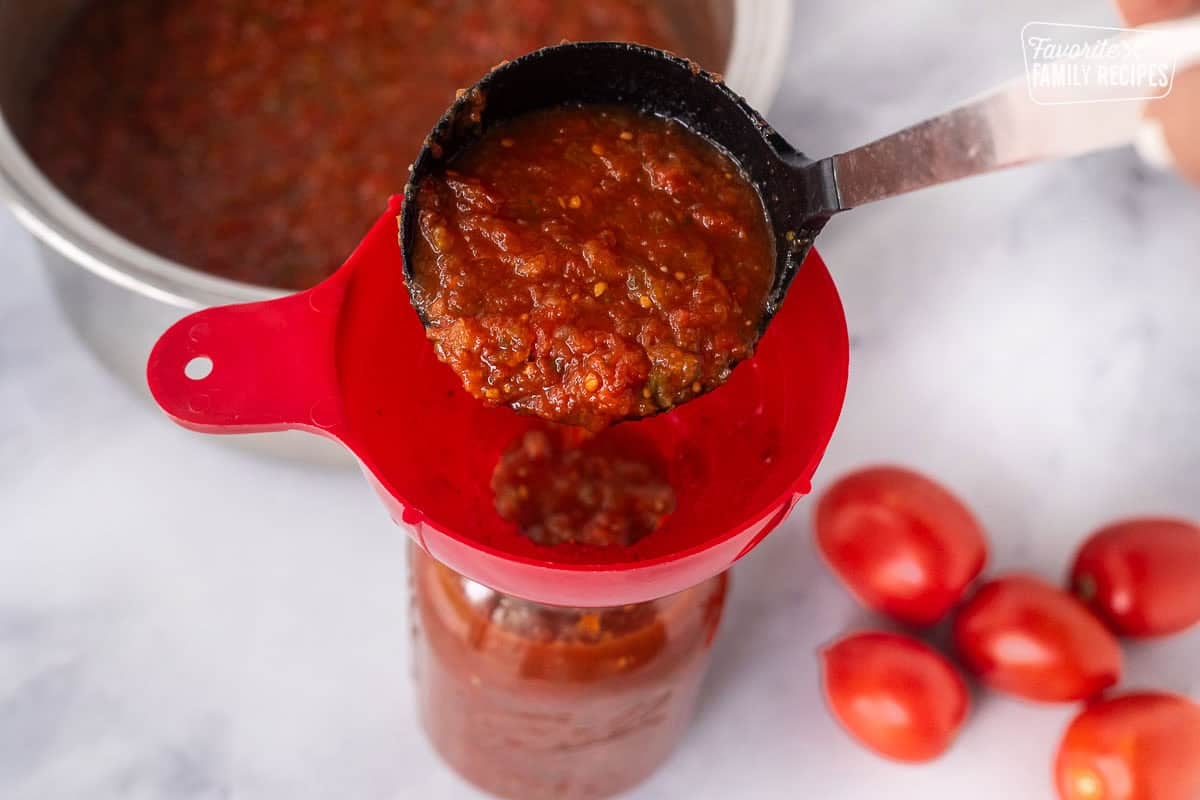 Using a ladle to pour sweet canned salsa into a canning jar with a canning funnel.