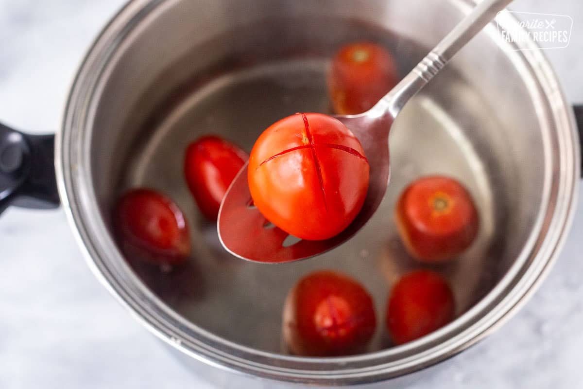 Tomato lifted from a hot pot of boiling water with a slotted spoon.