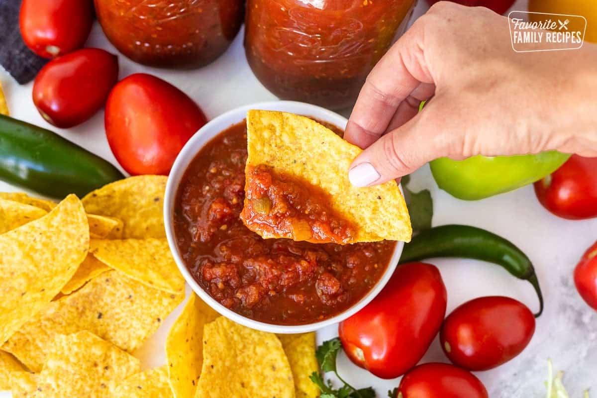 Tortilla chip dipped in sweet canned salsa held over a bowl