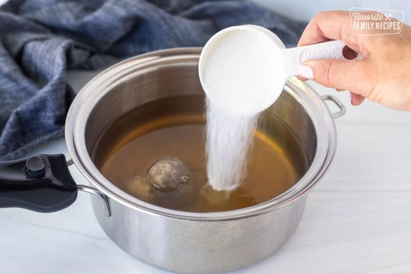 Pouring sugar into a saucepan with vinegar, sugar and spice bag.