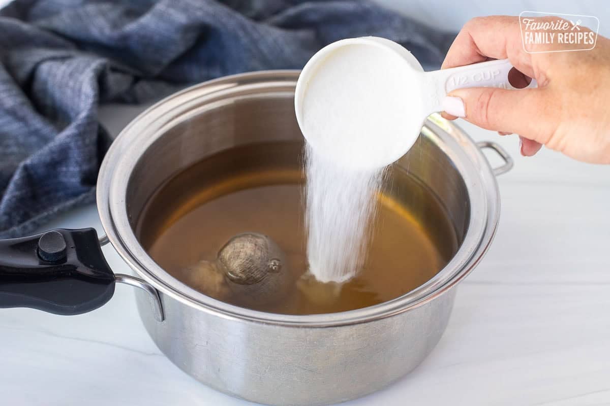 Pouring sugar into a saucepan with vinegar, sugar and spice bag.