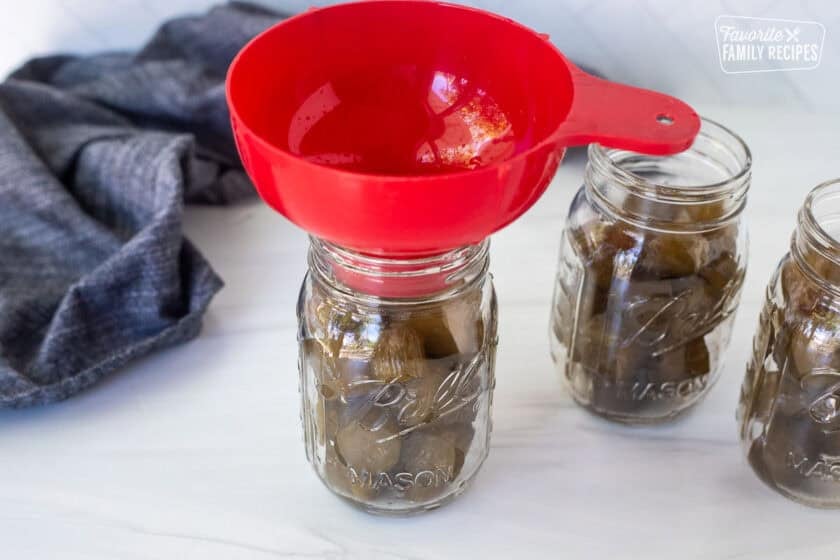 Pint jar with cut pickles and funnel on top.