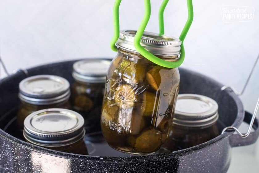Lifting a jar of sweet pickles out of canning pot with special tongs.