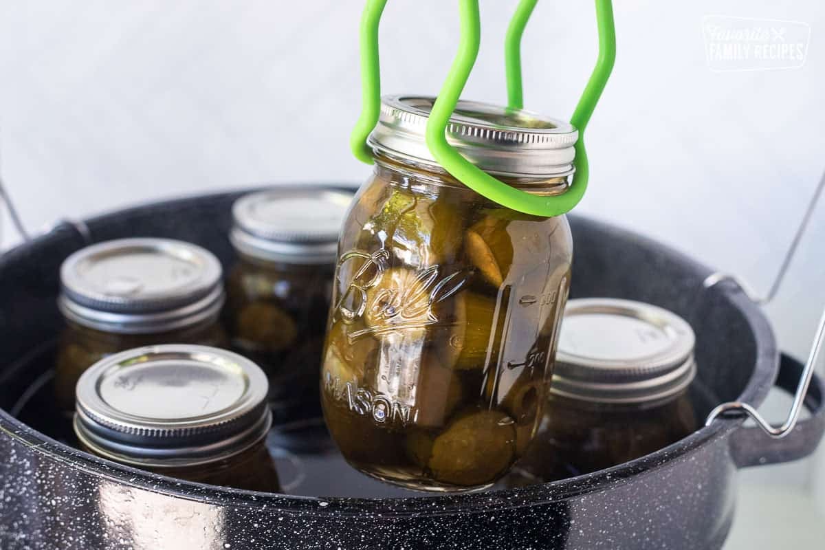 Lifting a jar of sweet pickles out of canning pot with special tongs.