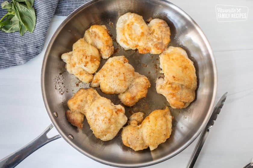 Skillet with golden browned chicken thighs and tongs on the side.