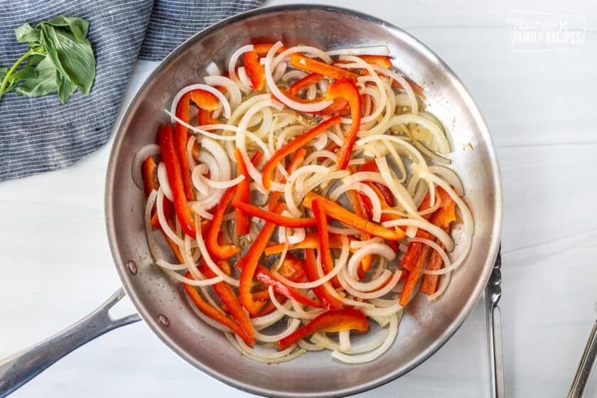 Skillet sautéing sliced onion, garlic and red peppers. Tongs on the side.
