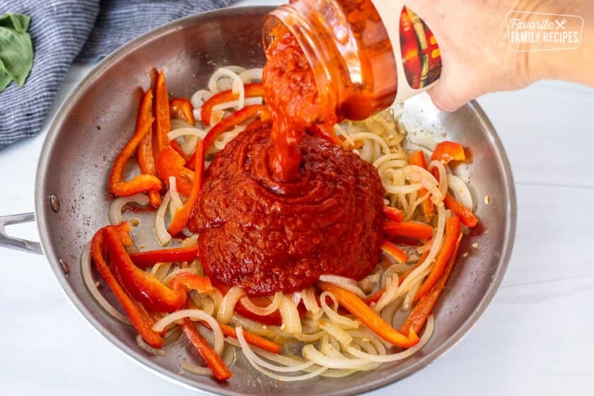 Pouring marinara sauce into sautéed onion and pepper mixture.