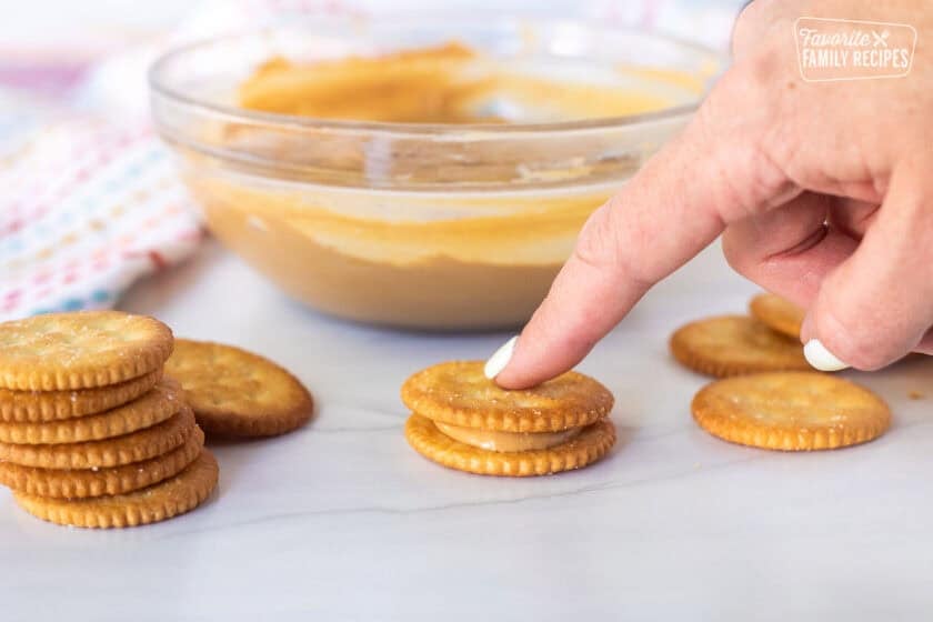 Pressing down Ritz cracker on top of another Ritz cracker with peanut butter filling.