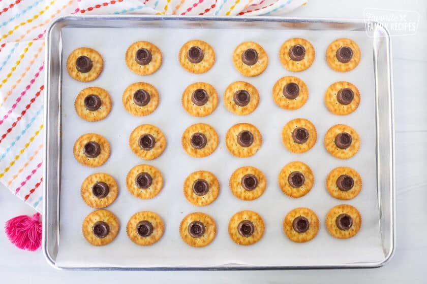 Rolos placed on top of Ritz crackers lined up on parchment paper.