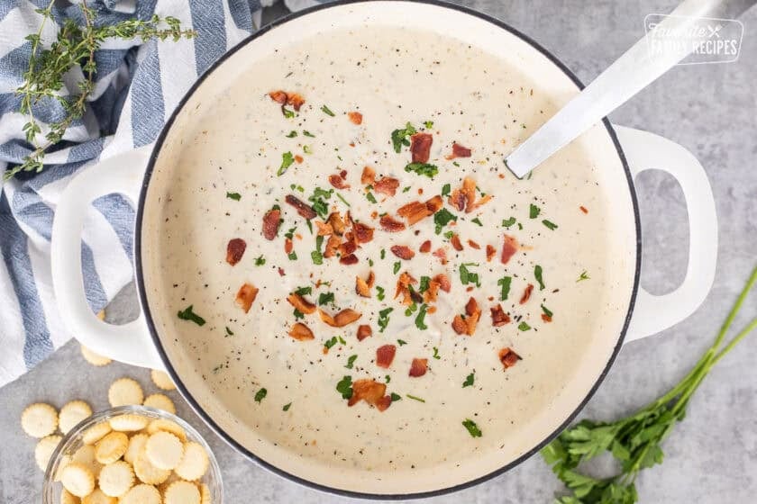 Ladle resting in a pot full of clam chowder with fresh clams and garnished with bacon, pepper and fresh parsley.