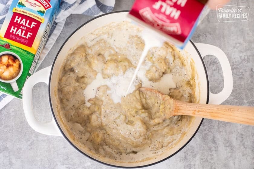 Pouring half and half into a pot with thick clam chowder mixture.