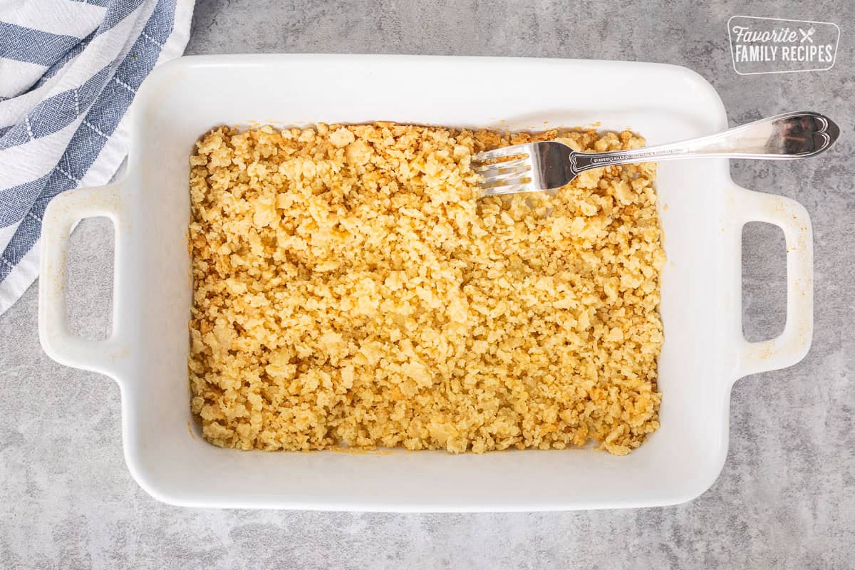 Using a fork to break up the baked flour butter mixture in a baking dish.