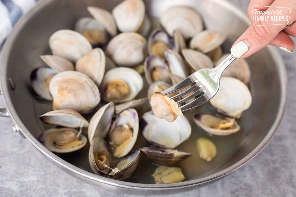 Fork with clam meat above skillet of opened clams.