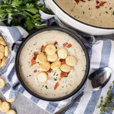 Bowl of clam chowder with fresh clams and garnished with bacon, crackers, pepper and fresh parsley.