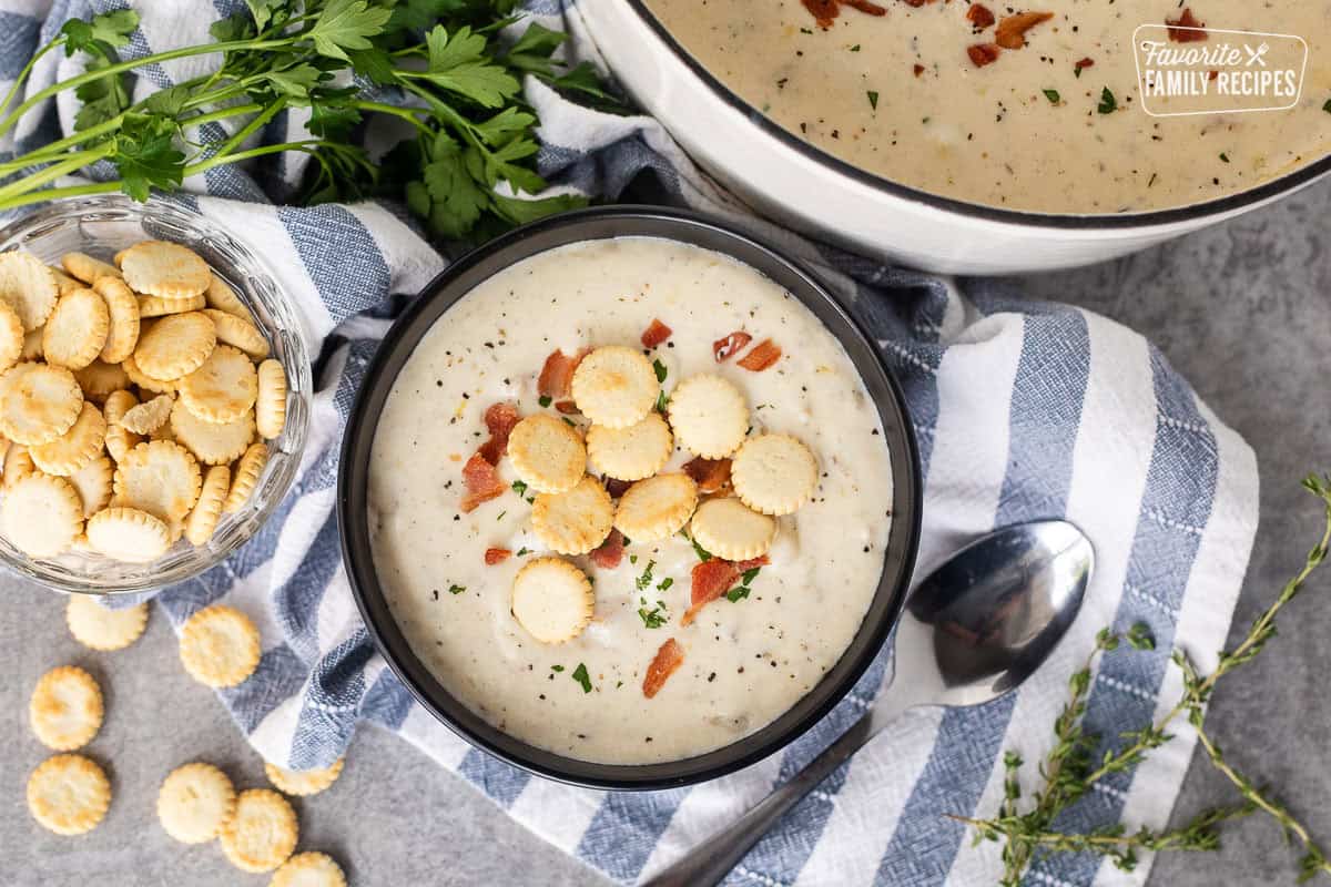 Bowl of clam chowder with fresh clams and garnished with bacon, crackers, pepper and fresh parsley.