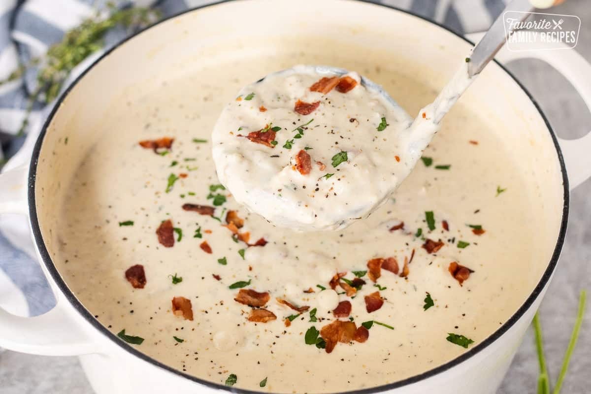 Ladle full of clam chowder with fresh clams and garnished with bacon, pepper and fresh parsley.